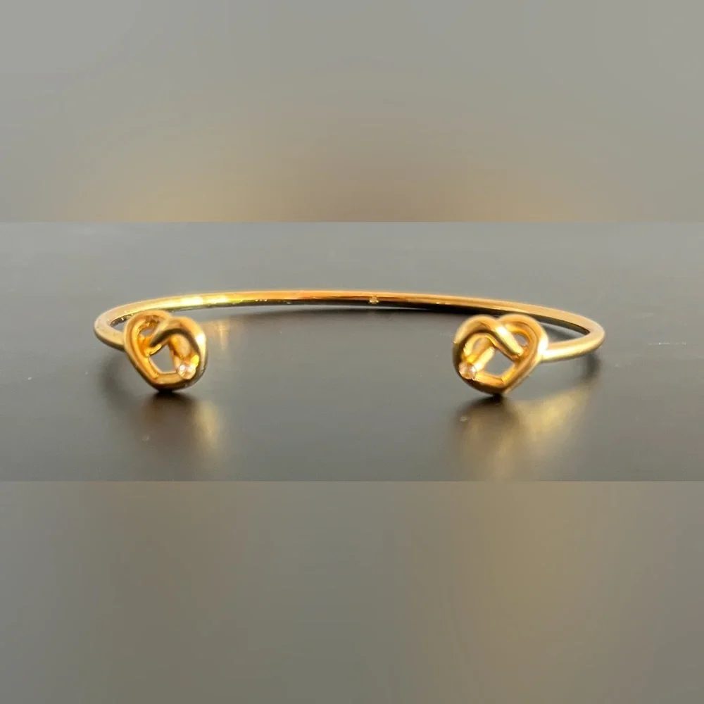 Kate Spade New York Loves Me Knot Cuff bangle in gold-tone w knot-accented ends.